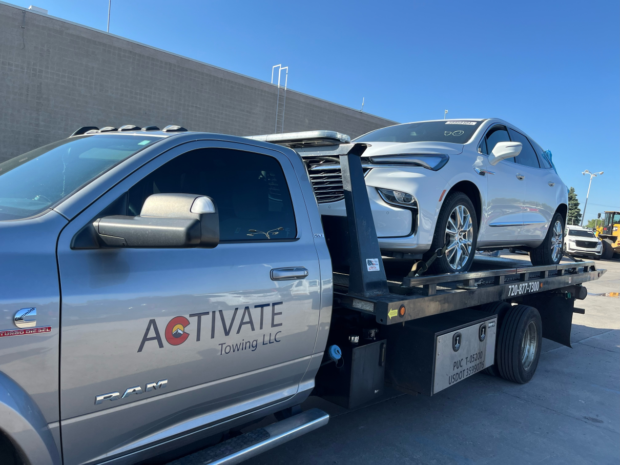Activate Towing flatbed transporting a white Buick Enclave SUV in Parker, Colorado