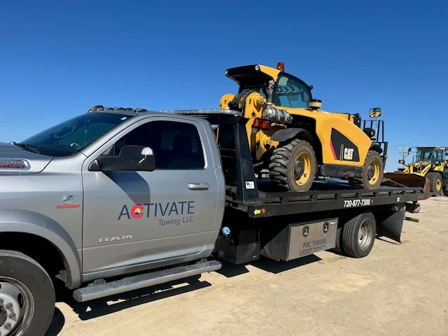 Activate Towing flatbed hauling a CAT skid steer. Heavy equipment transport across the Front Range