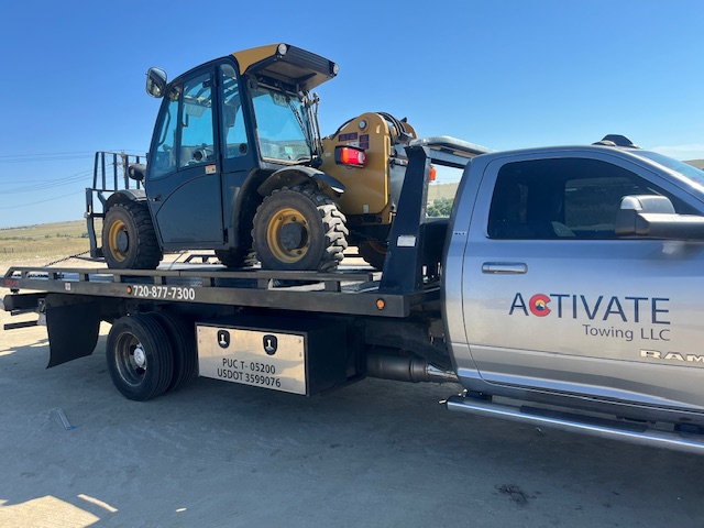 Activate Towing flatbed hauling a JCB telehandler. Medium-duty equipment transport in Colorado